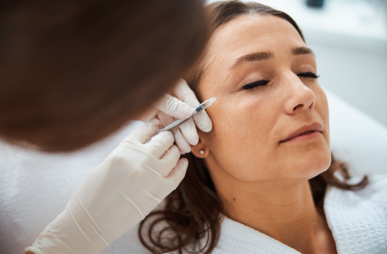 A practitioner carefully injects Botox around a patient's eyes.